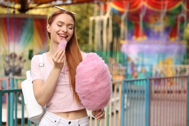 Photo of Beautiful woman eating cotton candy at funfair. Space for text