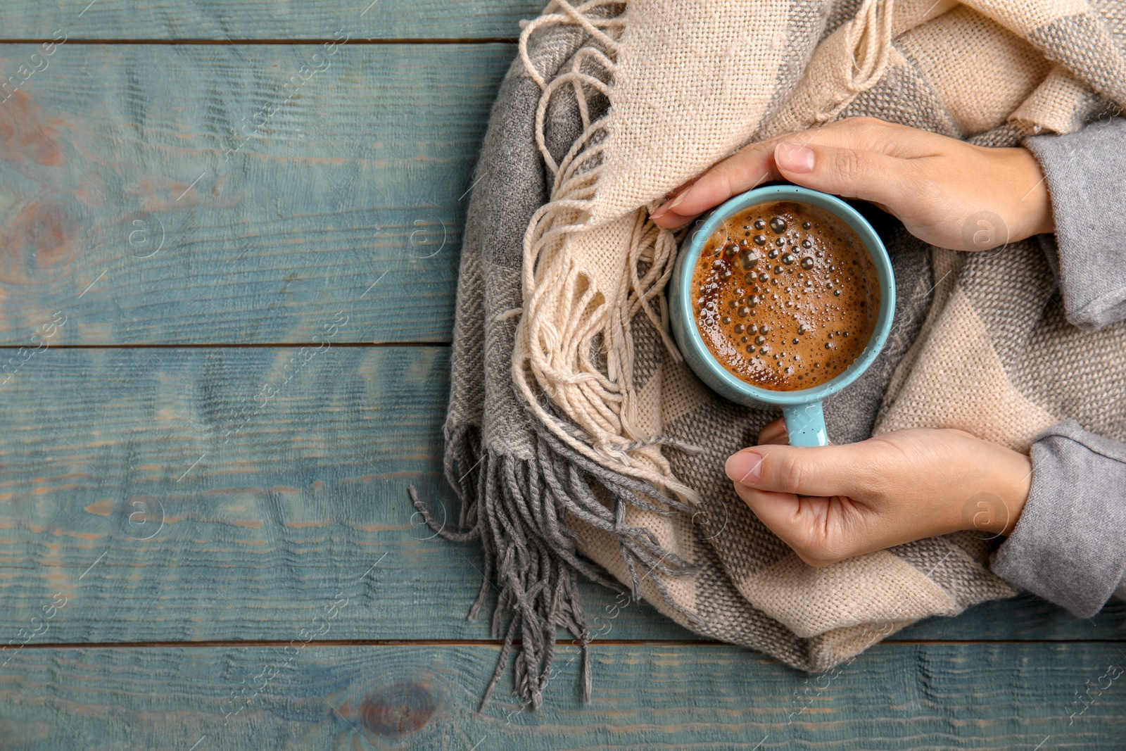 Photo of Woman with warm scarf holding cup of hot winter drink on wooden background, top view. Space for text