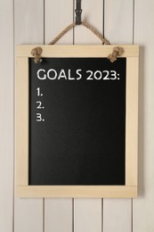 Image of Blackboard with phrase GOALS 2023 and empty checklist on hanging on white wooden background