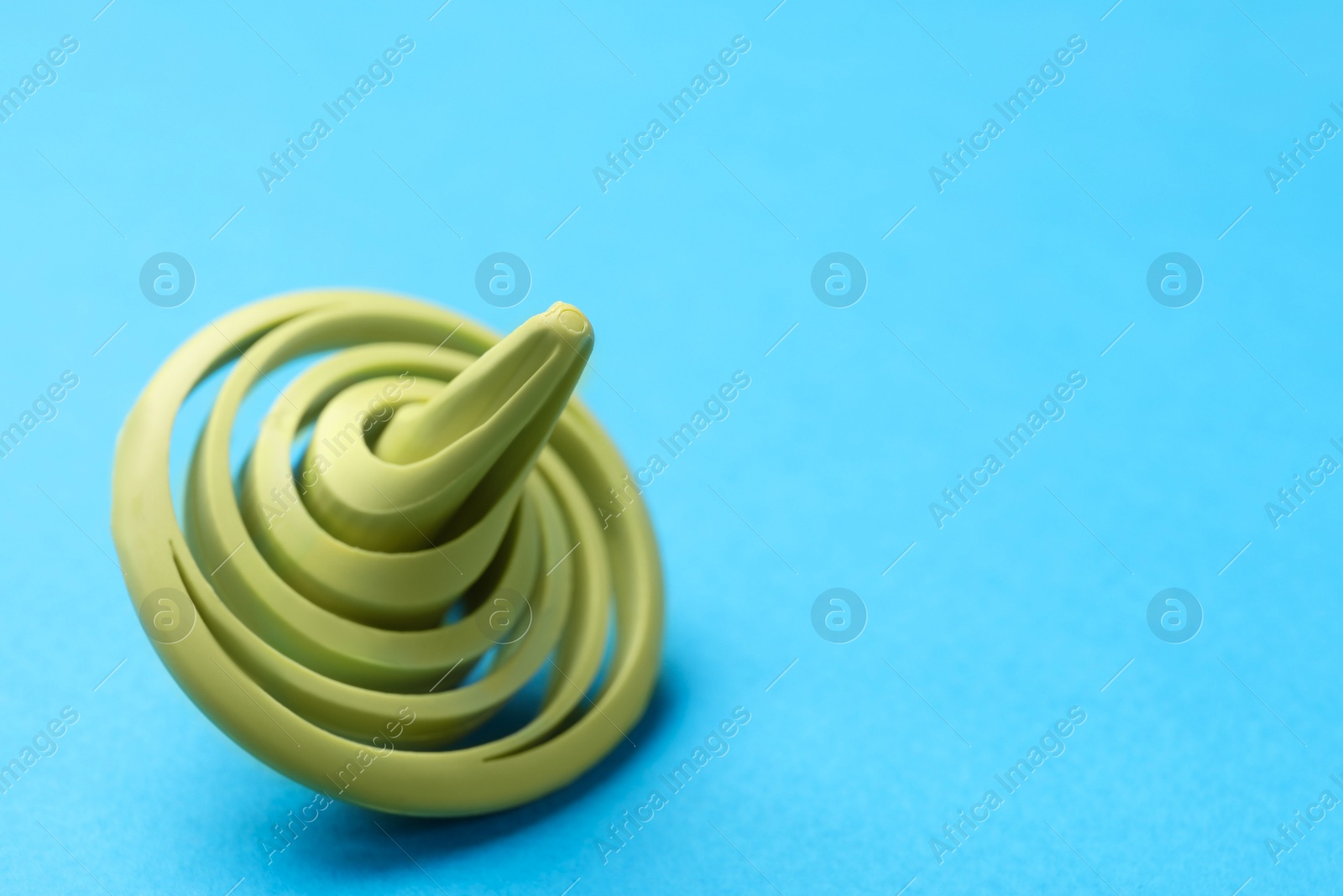 Photo of One green spinning top on light blue background, closeup. Space for text