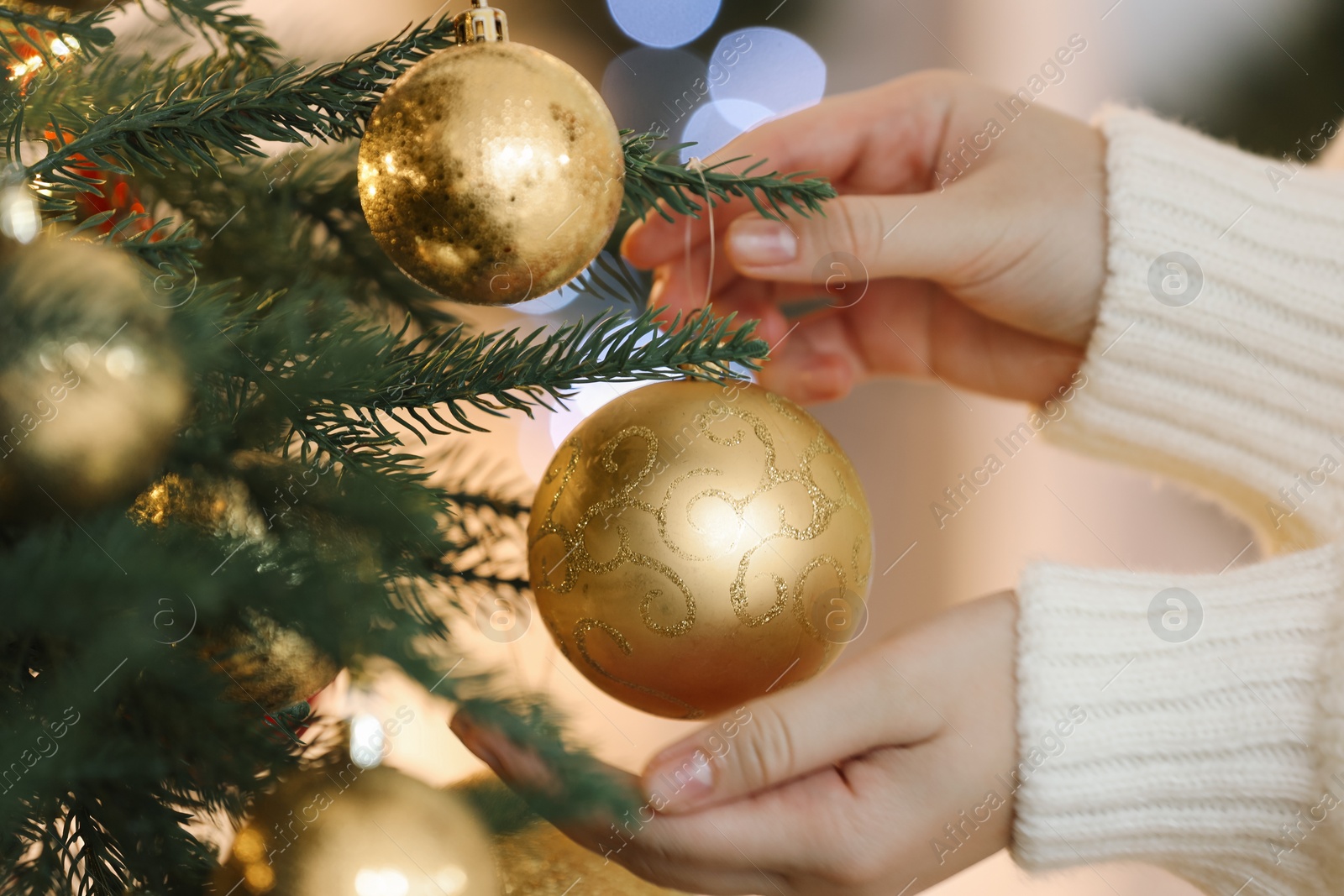 Photo of Woman decorating Christmas tree with golden festive ball on light background, closeup