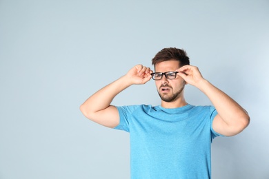 Photo of Young man with vision problems wearing glasses on grey background, space for text