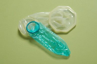 Photo of Unrolled female and male condoms on light olive background. Safe sex