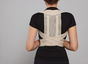 Photo of Closeup of woman with orthopedic corset on grey background, back view. Space for text