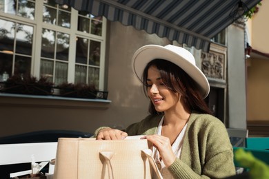 Young woman with stylish bag at table in outdoor cafe