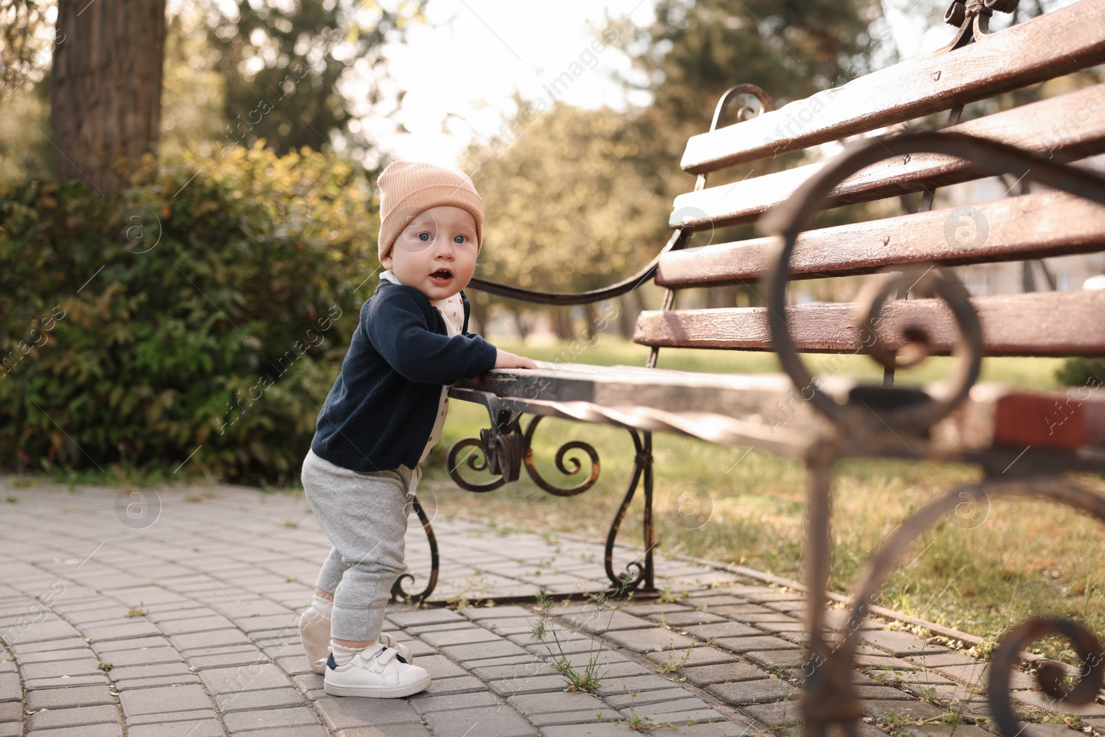 Photo of Little baby learning to walk near bench in park