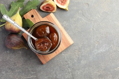 Photo of Jar of tasty sweet jam, fresh figs and green leaf on grey table, flat lay. Space for text
