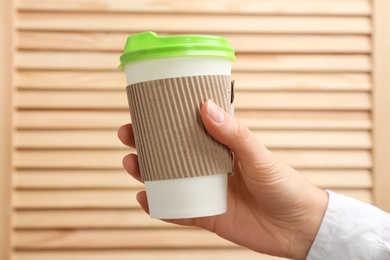 Photo of Woman holding takeaway paper coffee cup on wooden background