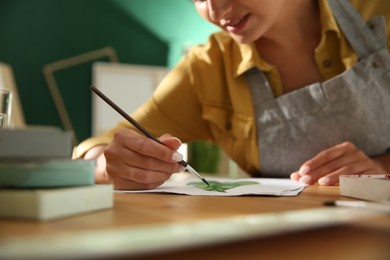 Young woman drawing leaf at table indoors, closeup