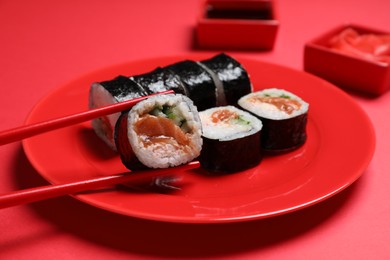 Tasty sushi rolls and chopsticks on red background, closeup