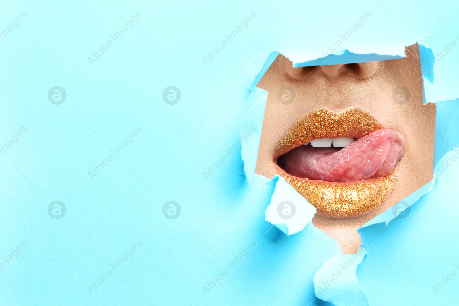 Photo of View of beautiful young woman with creative lips makeup through hole in color paper