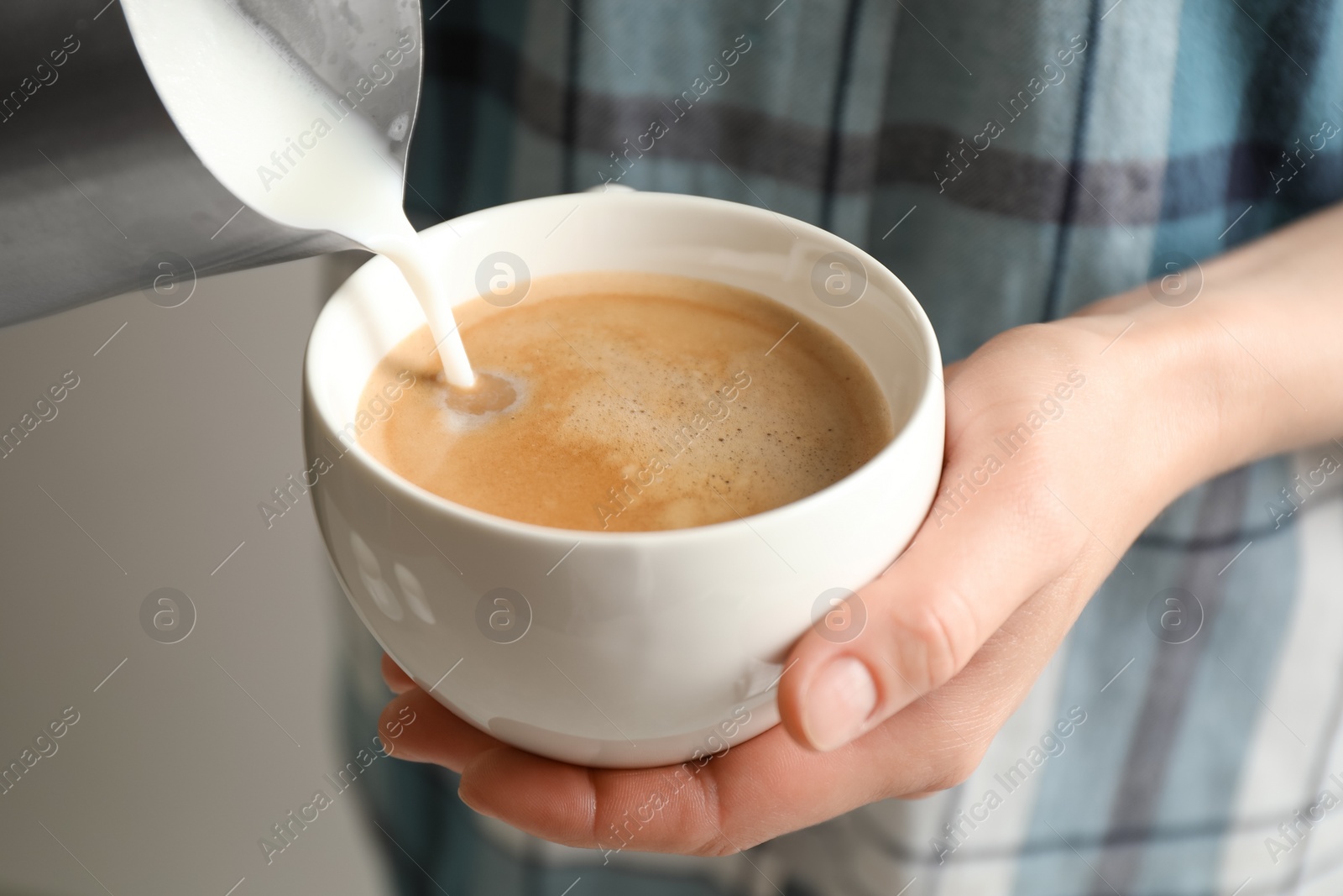 Photo of Woman pouring milk into cup of hot coffee, closeup