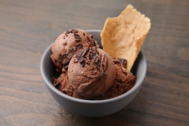 Photo of Tasty chocolate ice cream and piece of waffle cone in bowl on wooden table, closeup