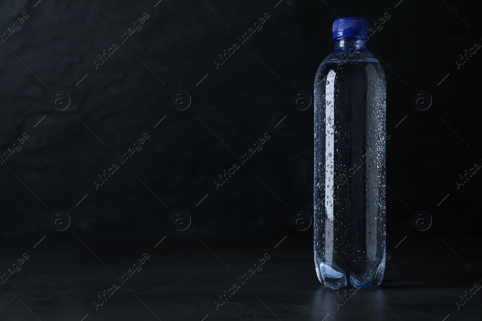 Photo of Plastic bottle with water on black background, space for text