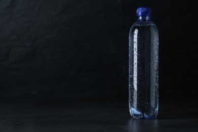 Plastic bottle with water on black background, space for text