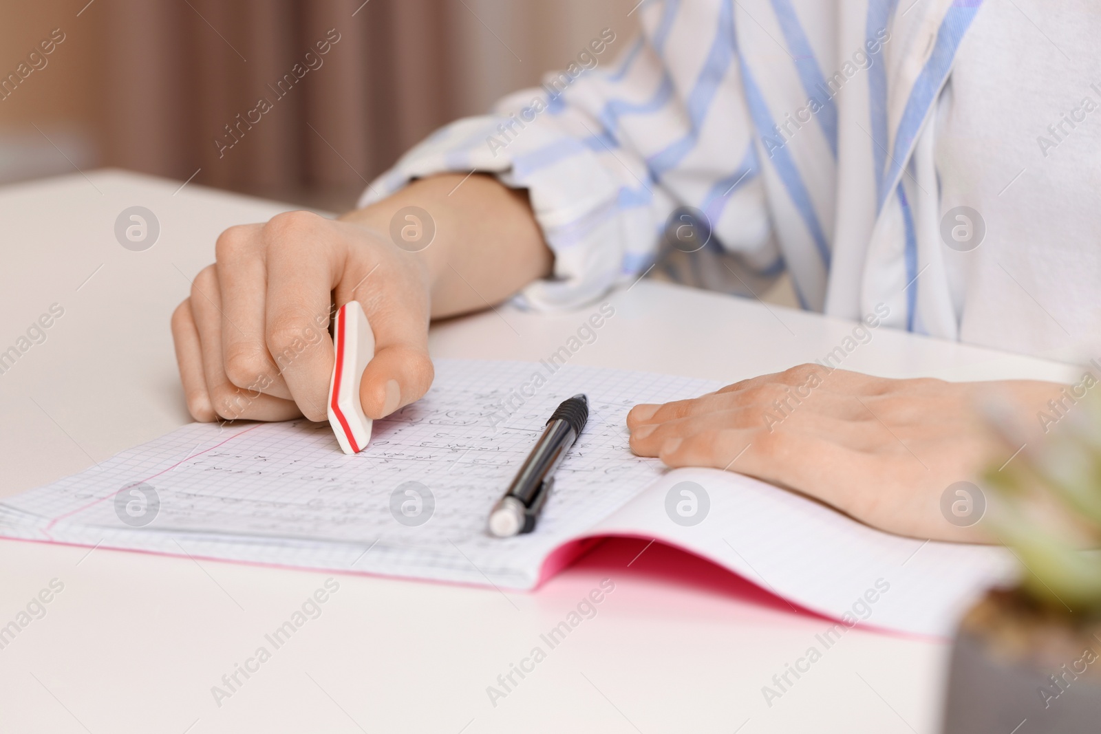 Photo of Girl erasing mistake in her notebook at white desk, closeup