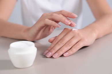 Photo of Young woman applying hand cream at table, closeup