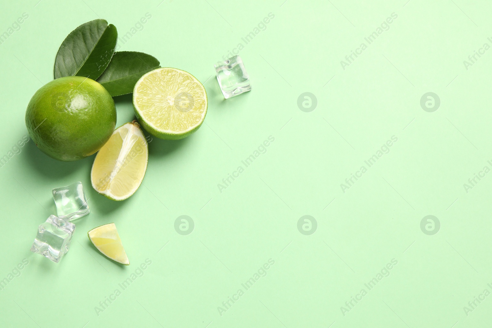 Photo of Fresh ripe limes with leaves and ice cubes on light green background, flat lay