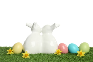 Photo of Ceramic Easter bunnies and dyed eggs on green grass against white background