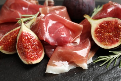 Delicious ripe figs and prosciutto served on black table, closeup