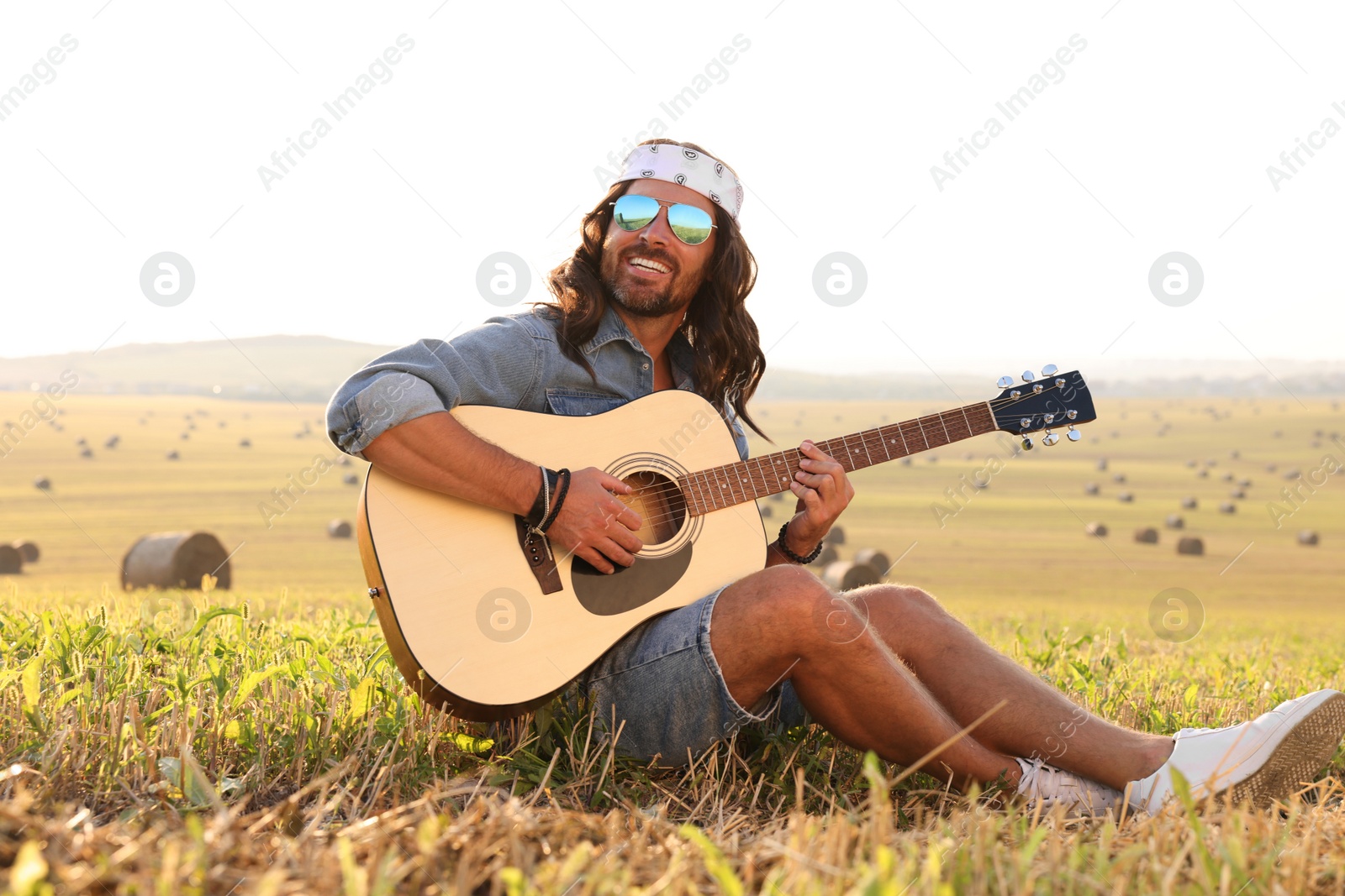 Photo of Handsome happy hippie man playing guitar in field