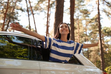 Photo of Enjoying trip. Happy young woman leaning out of car window, low angle view