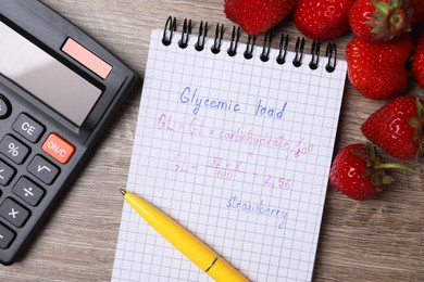 Photo of Notebook with calculated glycemic load for strawberry, calculator, pen and fresh berries on wooden table, flat lay