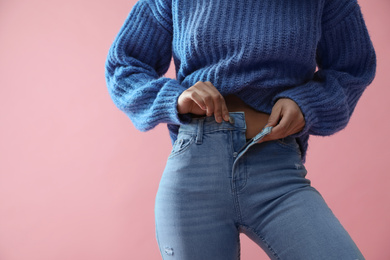 Photo of Woman unbuttoning jeans on pink background, closeup