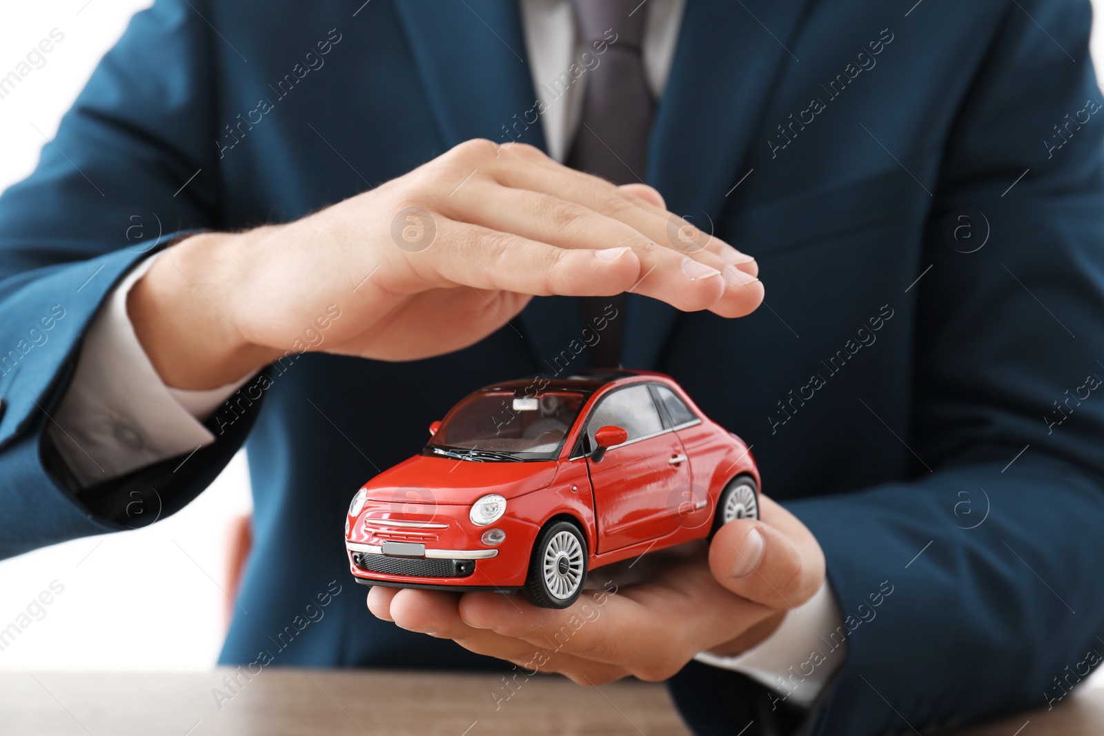 Photo of Insurance agent holding toy car over table, focus on hands