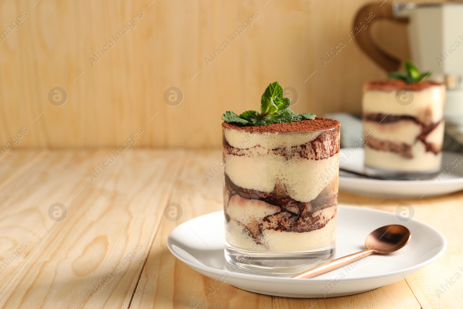 Photo of Tasty tiramisu and mint in glasses on light wooden table, space for text