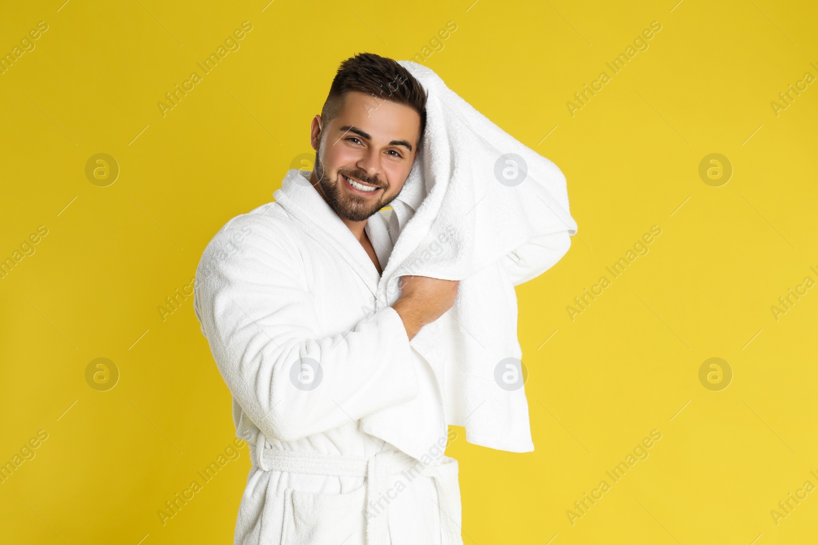 Photo of Young man in bathrobe drying hair with towel on yellow background