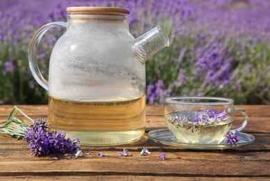 Tasty herbal tea and fresh lavender flowers on wooden table in field