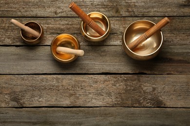 Photo of Golden singing bowls and mallets on wooden table, flat lay. Space for text