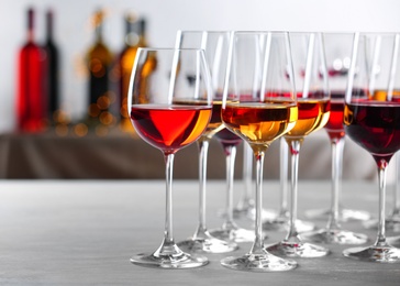 Glasses with different wines on table against blurred background. Space for text