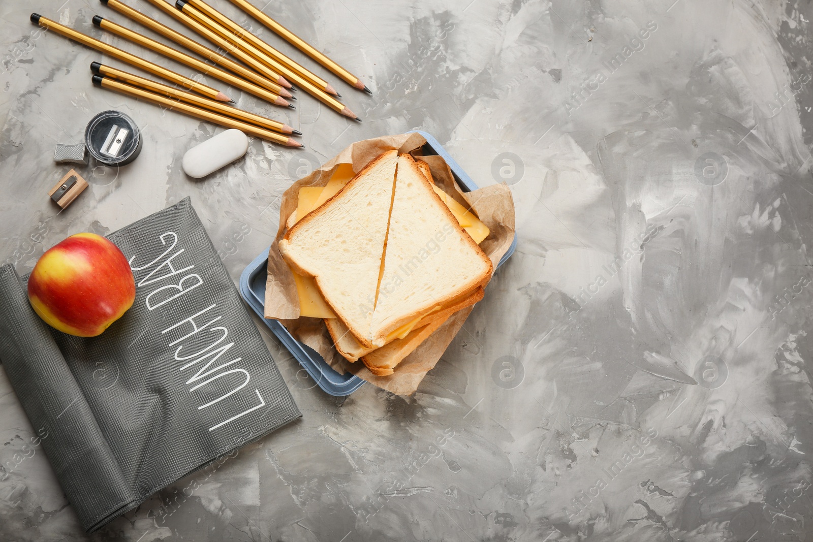 Photo of Flat lay composition with lunch box, tasty sandwich and stationery on grey background