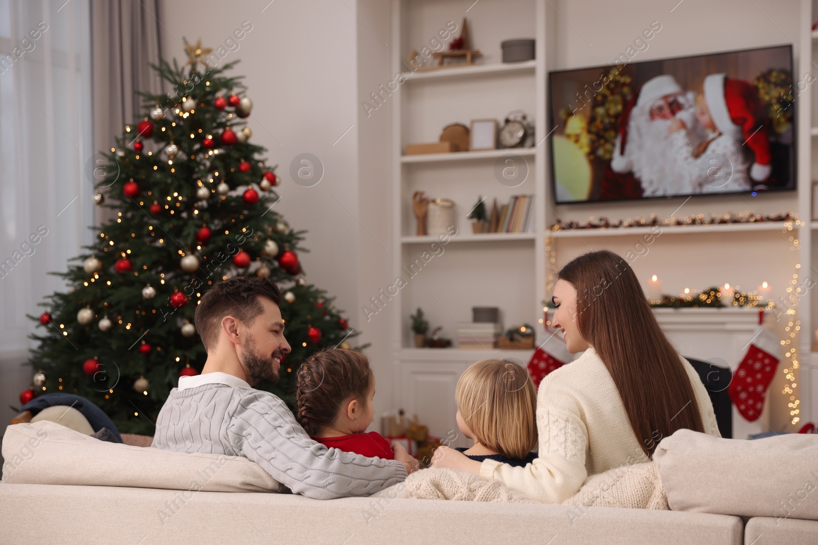 Photo of Happy family spending time on sofa near TV in cosy room, back view. Christmas atmosphere