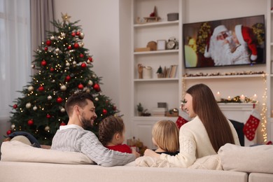 Photo of Happy family spending time on sofa near TV in cosy room, back view. Christmas atmosphere