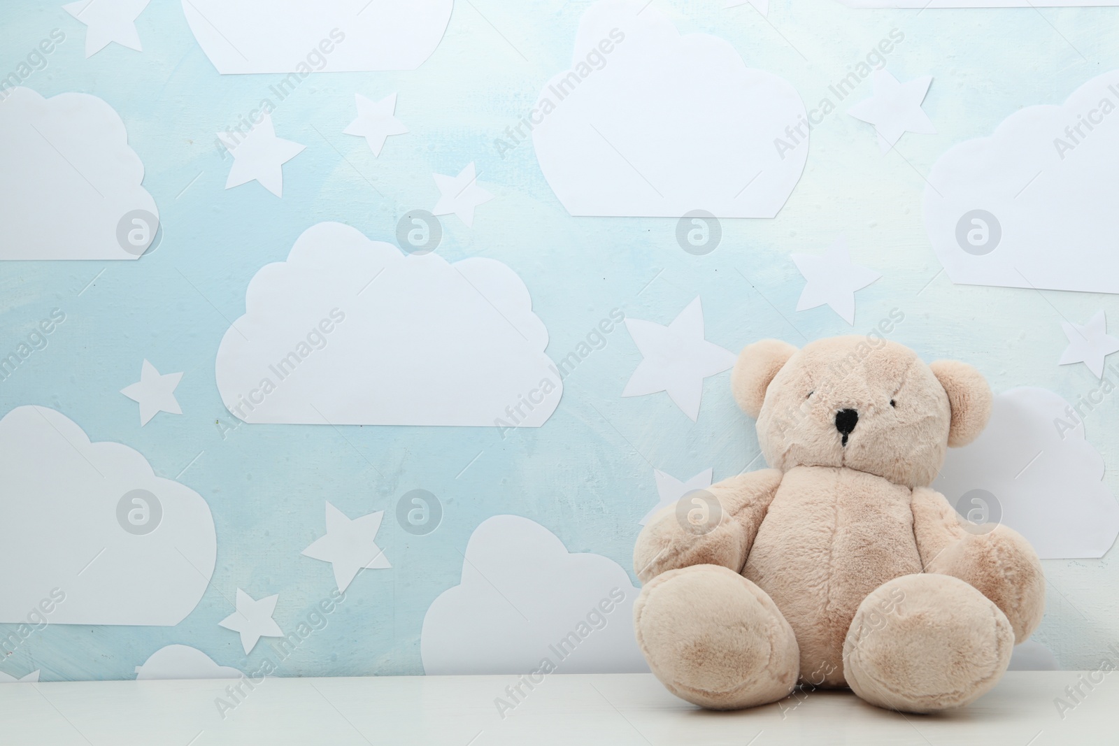 Photo of Teddy bear on white table near wall with blue sky, space for text. Baby room interior