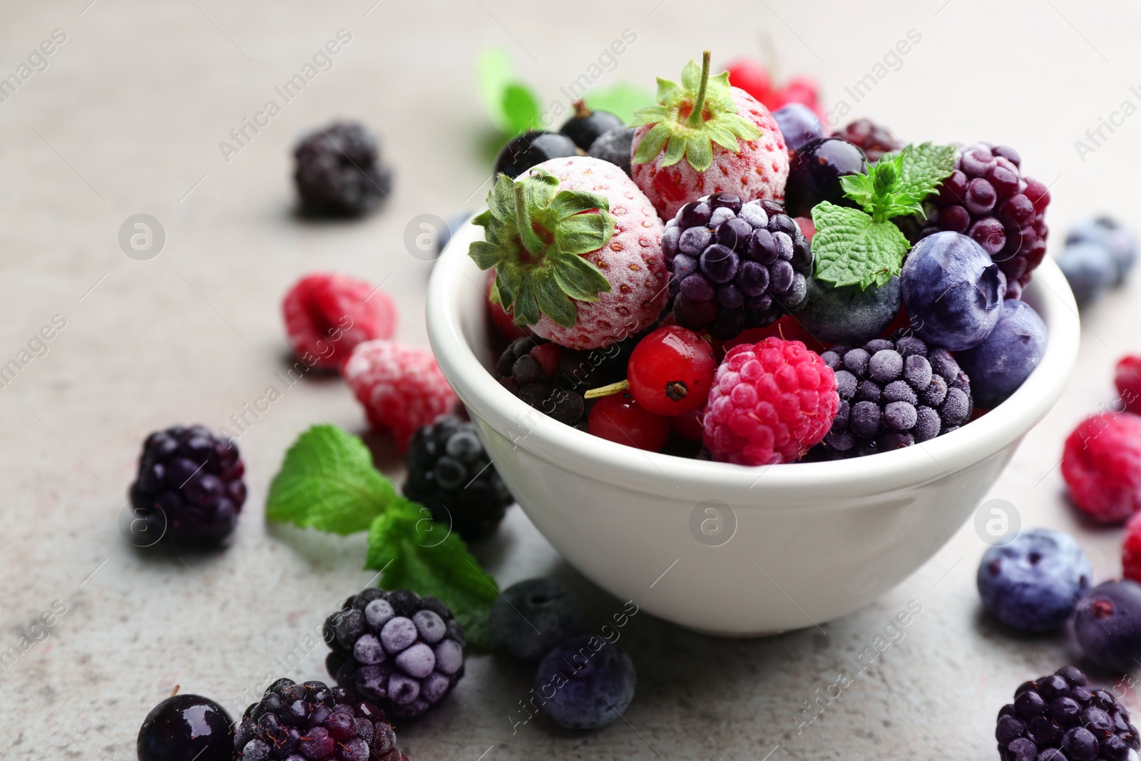 Photo of Mix of different frozen berries on grey table, closeup. Space for text