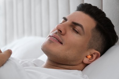 Photo of Man with foam ear plugs sleeping in bed, closeup