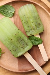 Photo of Tasty kiwi ice pops on wooden plate, top view. Fruit popsicle