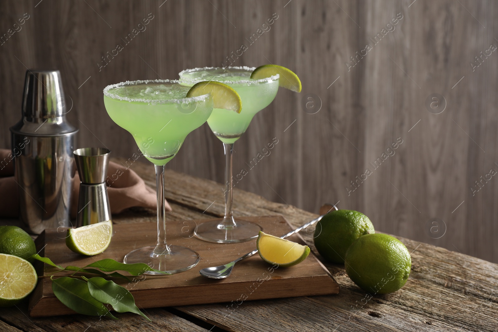 Photo of Delicious Margarita cocktail in glasses, limes and bartender equipment on wooden table