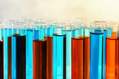 Many test tubes with different liquid samples on color background, closeup