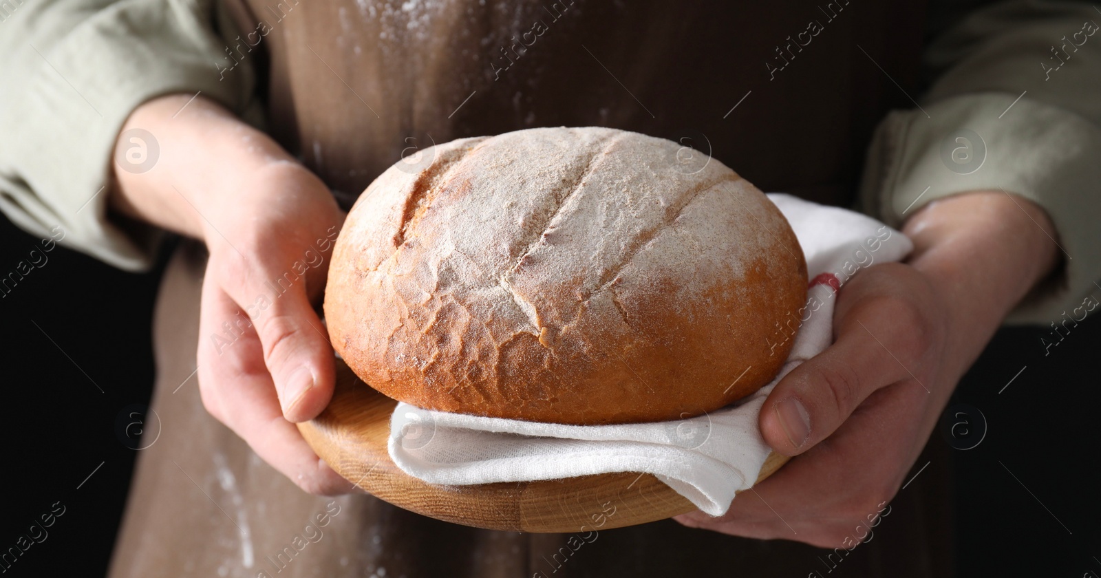 Photo of Woman holding freshly baked bread on black background, closeup