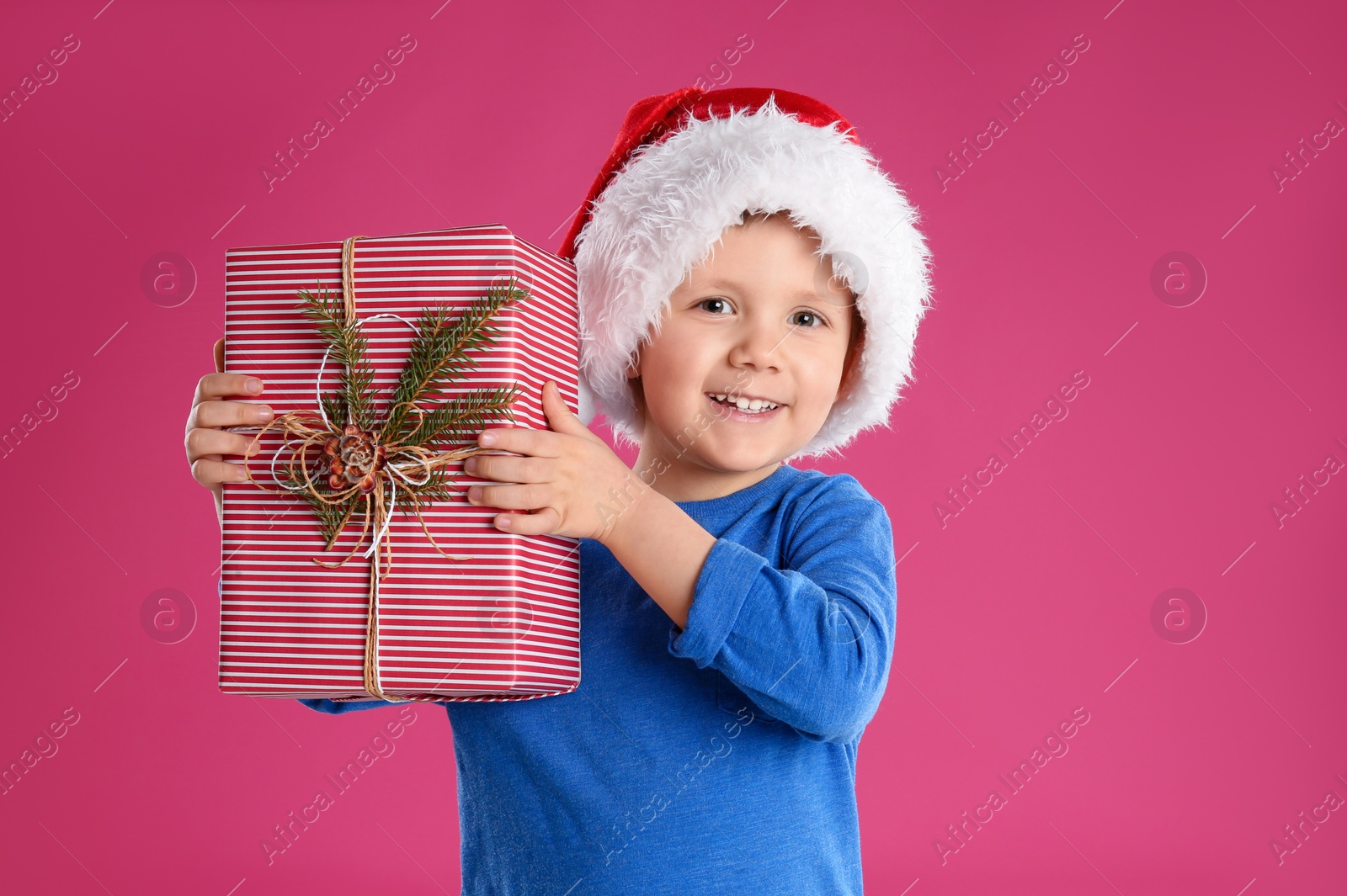 Photo of Cute child in Santa hat with Christmas gift on pink background