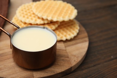 Photo of Tasty condensed milk and waffles on wooden table, closeup. Space for text