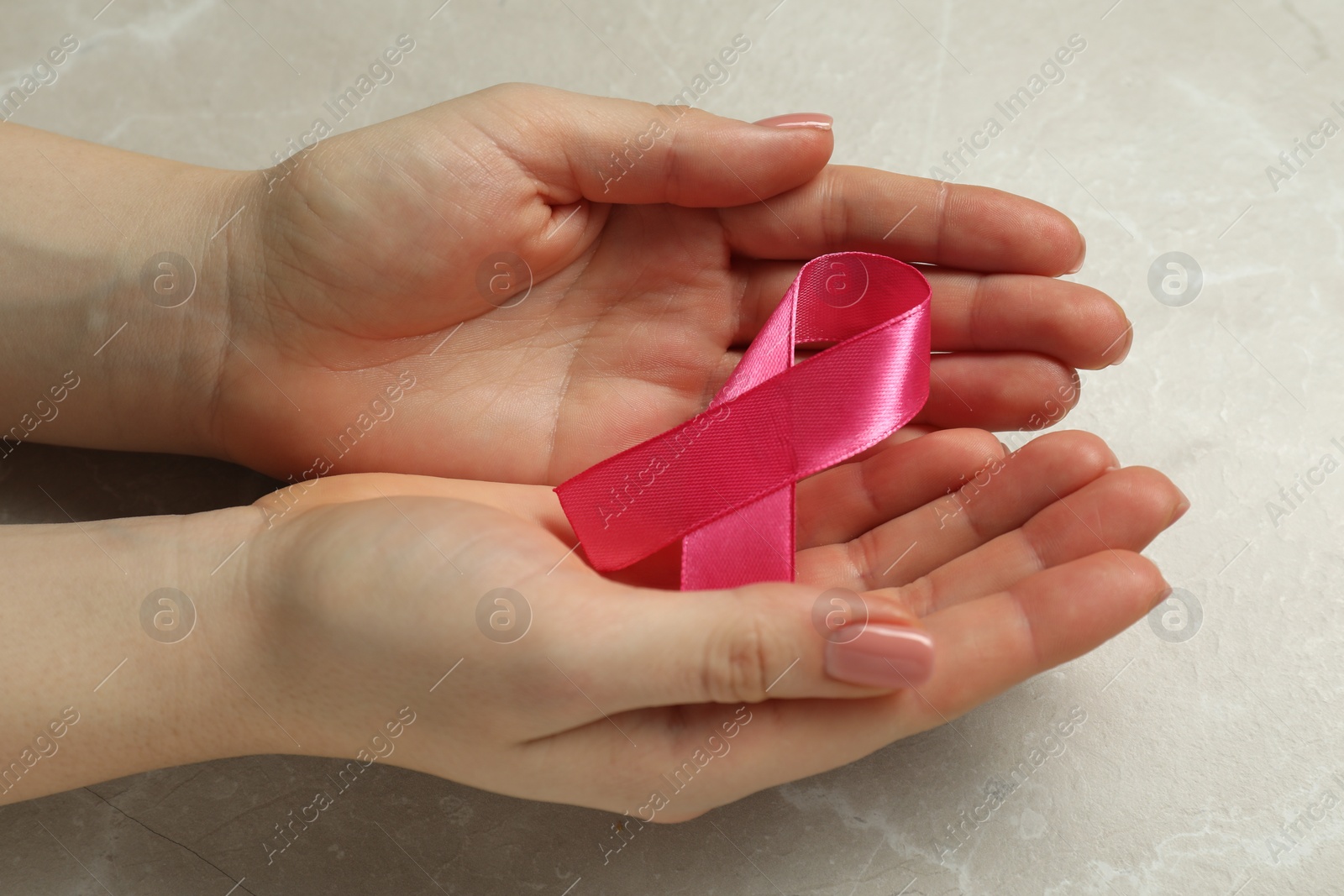 Photo of Breast cancer awareness. Woman with pink ribbon at light grey table, closeup