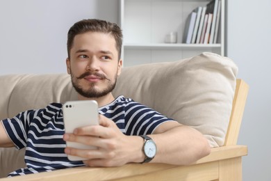 Photo of Man with smartphone on beige sofa in cozy room
