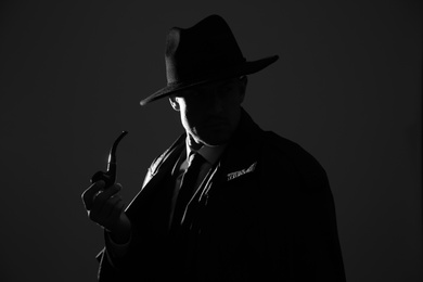 Photo of Old fashioned detective with smoking pipe on dark background, black and white effect