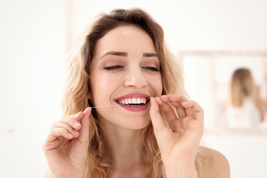 Photo of Young woman flossing her teeth indoors